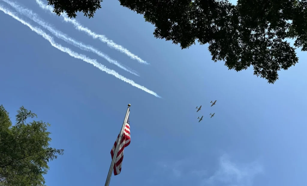 Four aircraft perform a flyover above an American flag during the Flags & Honor of Minnesota Car Show opening ceremony.